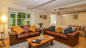 A cozy living room with two leather sofas, a wooden coffee table, and a dining area with a table set for four. - Pentre Court Cottage (Abergavenny)