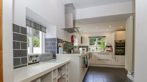 A modern kitchen with white cabinetry, a built-in oven, and a window providing natural light. - Pentre Court Cottage (Abergavenny)