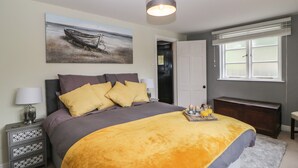 Una camera da letto con un letto, un comodino, una lampada, un quadro, una porta, una finestra e una panca.