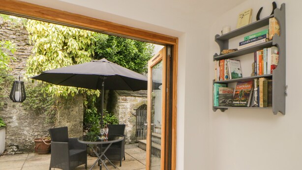 Patio aperto con tavolo e sedie sotto un ombrellone grande, una libreria con libri e un muro in pietra sullo sfondo.