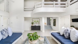 A spacious living area with a high ceiling, a central seating area with blue sofas, a coffee table with a plant, and a staircase leading to an upper level. - Closest villa in Casa to Minitas Beach with private pool, garden, screened patio (La Romana)