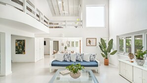 A spacious, well-lit living area with a high ceiling, a blue sofa, white cabinets, and large windows. - Closest villa in Casa to Minitas Beach with private pool, garden, screened patio (La Romana)