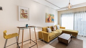Een moderne woonkamer met een gele bank, een glazen salontafel en een eethoek met een glazen tafel en stoelen.
