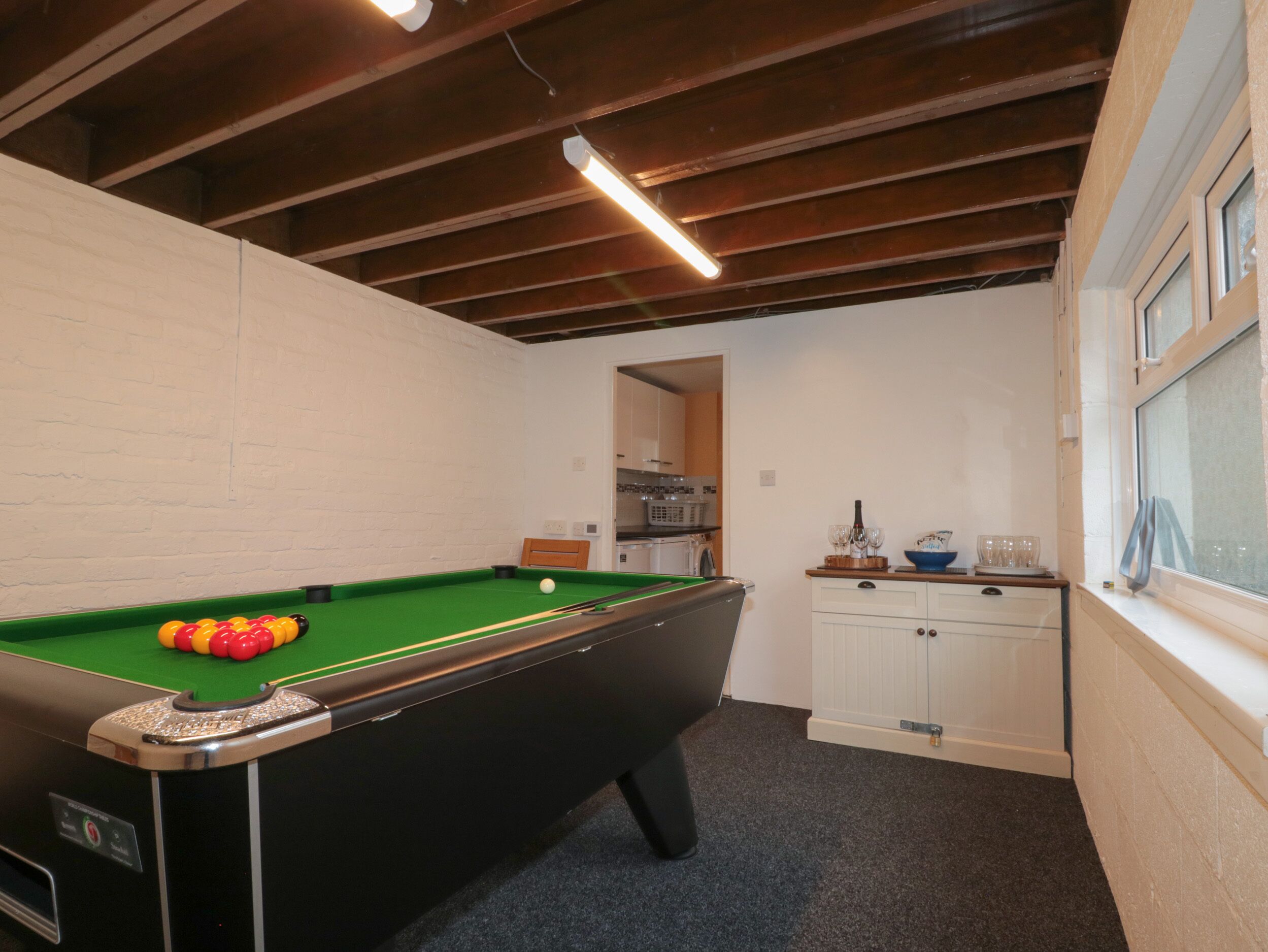 Una mesa de billar con bolas, una zona de cocina y un ventanal con cortinas.