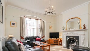 A living room with a sofa, television, fireplace, and a chandelier. - 50 West Street Edelweiss (Scarborough)
