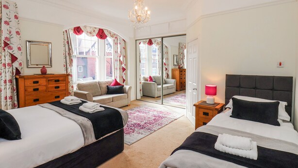 A bedroom with two beds, a dresser, a mirror, and a chandelier. - 50 West Street Edelweiss (Scarborough)
