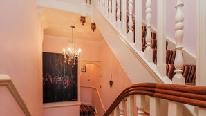A staircase with white balusters and a wooden handrail, leading to a room with a cityscape painting and a chandelier. - 50 West Street Edelweiss (Scarborough)