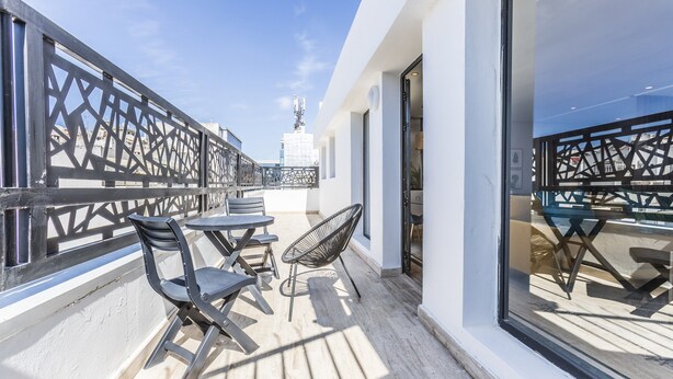 Ein Balkon im Freien mit Tisch und Stühlen, einem Geländer und Blick auf ein Gebäude im Hintergrund.
