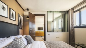 Ein modernes Schlafzimmer mit Bett, Nachttisch, einem Fenster mit Vorhängen und einer Tür zu einem anderen Raum.