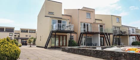 A modern residential building with multiple balconies, a paved courtyard, and a stone wall.