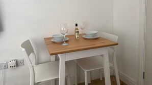 Une petite table à manger avec une bouteille de vin, deux verres à vin et deux bols posés sur une chaise blanche.