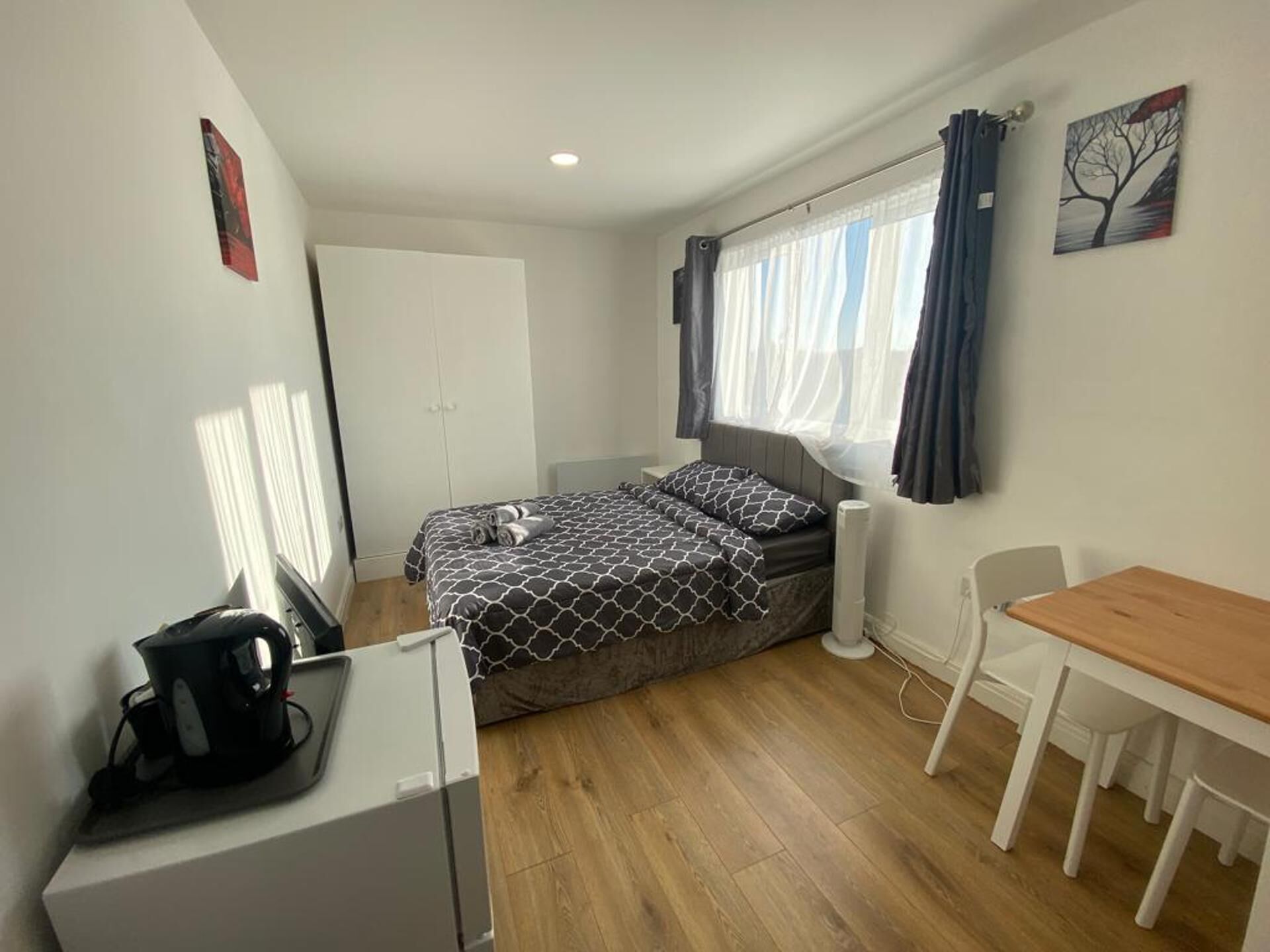 A compact room with a bed, a small desk, a chair, and a window with curtains.