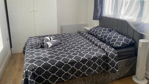 Une chambre à coucher comprenant un lit, une armoire, une table de chevet et une fenêtre avec des rideaux légers.