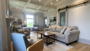 A spacious living room with a large sofa, a coffee table, and a blue armchair. - Thunderbird Farm - Luxury 5-Bedroom Farmhouse w/ Pool & Hands-On Farm Experience (Kawartha Lakes)