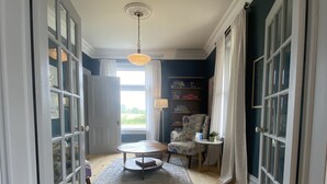 A hallway with wooden flooring, a round table with chairs, a lamp, and a ceiling light fixture. - Thunderbird Farm - Luxury 5-Bedroom Farmhouse w/ Pool & Hands-On Farm Experience (Kawartha Lakes)