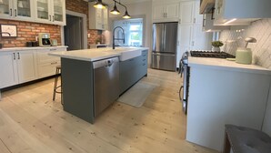 A modern kitchen with white cabinetry, a central island, stainless steel appliances, and a brick accent wall. - Thunderbird Farm - Luxury 5-Bedroom Farmhouse w/ Pool & Hands-On Farm Experience (Kawartha Lakes)