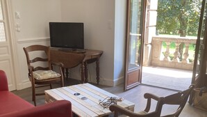 Een woonkamer met een houten salontafel, twee houten stoelen, een rode bank en een televisie op een houten dressoir.