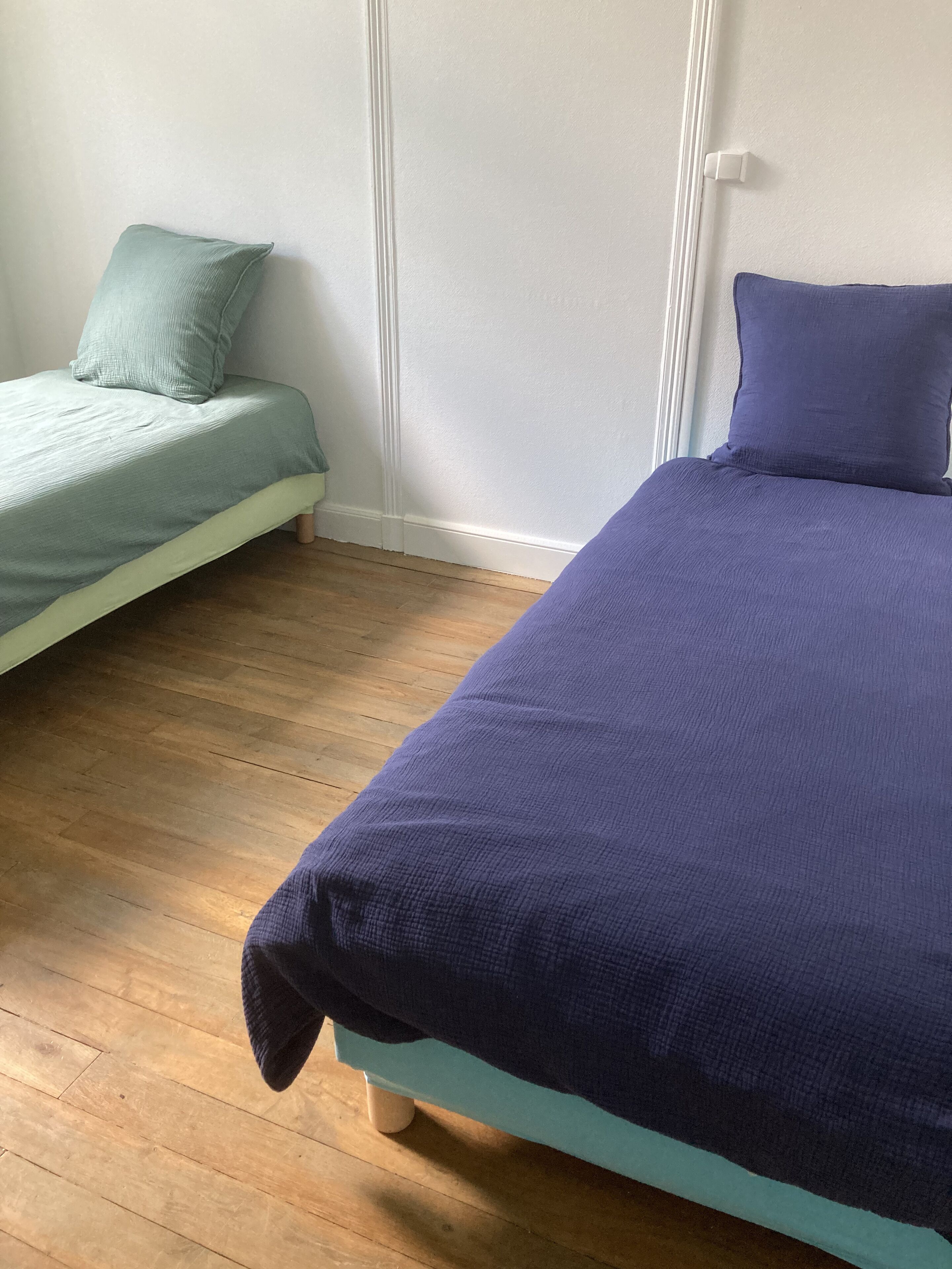 Een slaapkamer met twee bedden, waarvan één met een blauwgroene spreidek en de ander met een donkerblauwe.