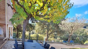 An outdoor dining area with a long table and chairs, surrounded by a garden and a building. - A l'ombre du chêne : Gîte Éden en Cévennes swimming pool, calm & nature at Anduze (Anduze)