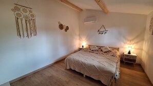 A bedroom with a wooden bed, two bedside tables with lamps, a wall-mounted air conditioner, and decorative wall hangings. - A l'ombre du chêne : Gîte Éden en Cévennes swimming pool, calm & nature at Anduze (Anduze)