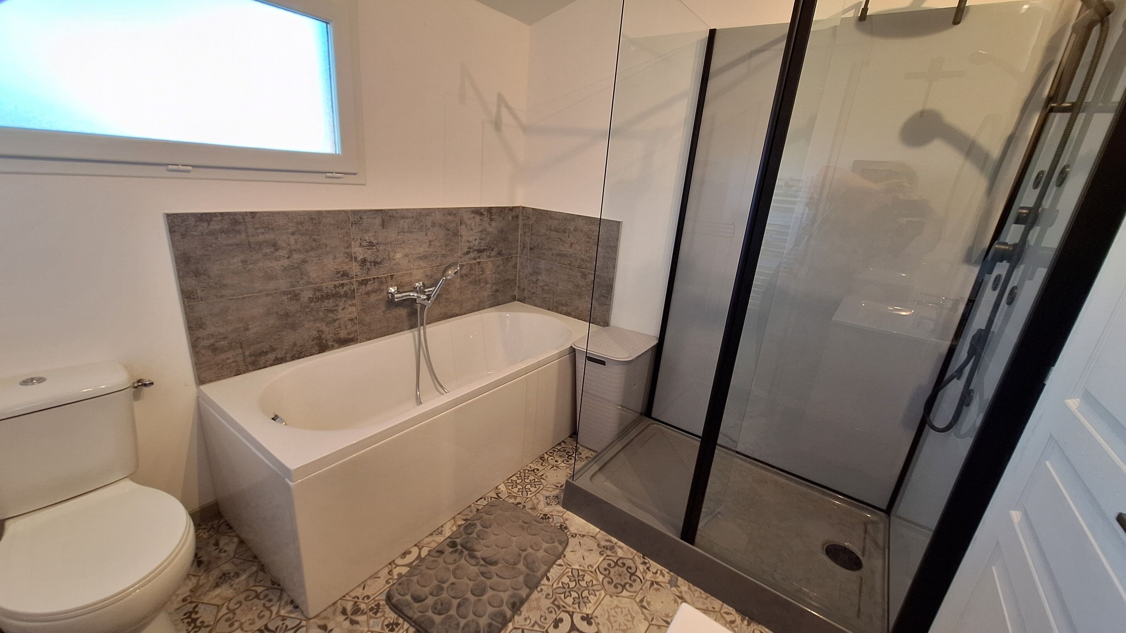 Een moderne badkamer met bad, toilet en glazen douchecabine.