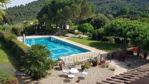 A rectangular swimming pool with a geometric tile pattern, surrounded by a gravel area with white metal chairs and tables. - Sous le grand pin: swimming pool and spa (Gîtes Eden en Cévennes) in Anduze (Anduze)
