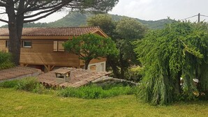 A wooden house with a tiled roof, surrounded by lush greenery and a hill in the background. - Sous le grand pin: swimming pool and spa (Gîtes Eden en Cévennes) in Anduze (Anduze)