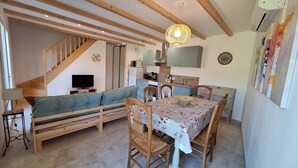 A cozy living room with a sofa, dining table, and chairs. A staircase leads to an upper level. - Sous le grand pin: swimming pool and spa (Gîtes Eden en Cévennes) in Anduze (Anduze)