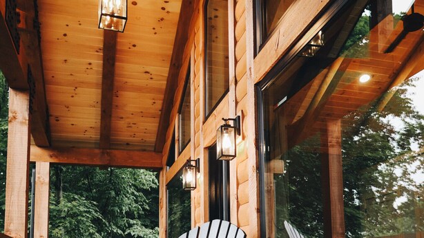 A wooden deck with Adirondack chairs and a table, large windows, and a hanging lantern.