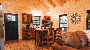 A cozy cabin interior with a wooden interior, a kitchen with a stove and microwave, a dining area with a table and chairs, and a brown leather couch.