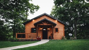 A wooden cabin with a porch, a pathway leading to the entrance, and a satellite dish on the right.