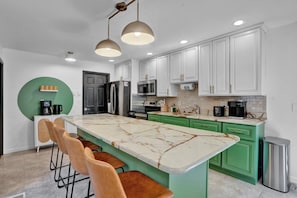 A modern kitchen with white cabinets, a large island with a marble countertop, and pendant lighting.