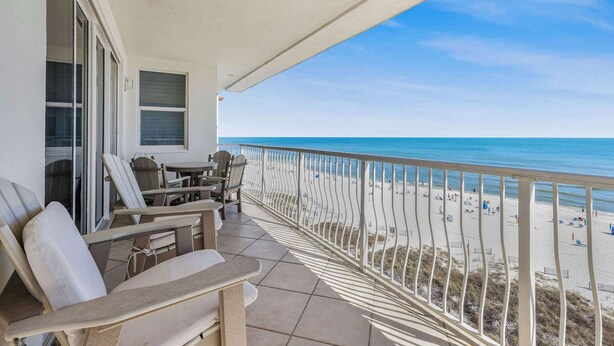 Un balcone con posti a sedere all'aperto, vista sulla spiaggia e cielo sereno.