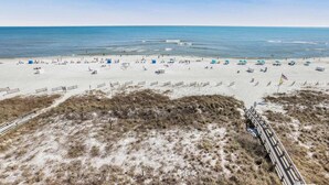 Una spiaggia con file di sdraio e ombrelloni, un sentiero sabbioso che conduce all'acqua, e bandierine che delimitano l'area spiaggia.