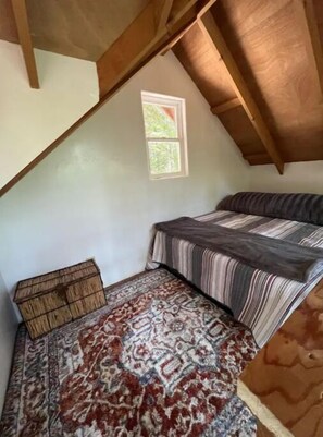 A small, sloped room with a bed, a window, and a patterned rug. - Jimmy’s Hike In cabin
 A tranquil retreat, family, and romantic getaway (Little River)