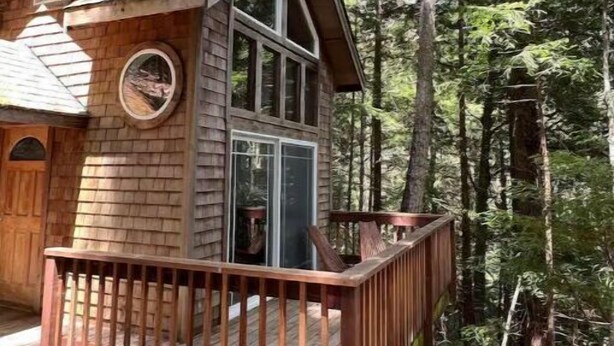 A cabin with a wooden deck, large windows, and a circular window on the side.