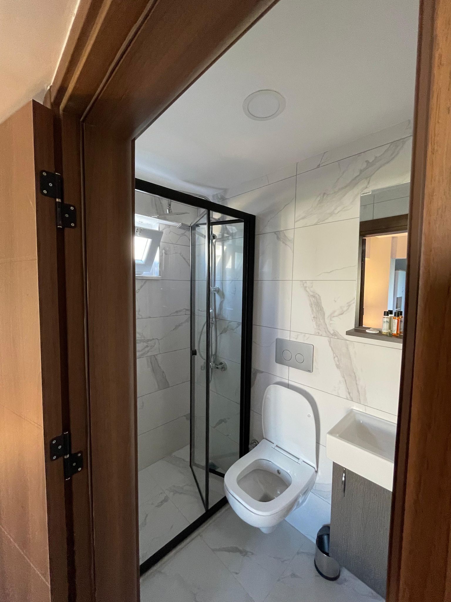 A modern bathroom with a glass-enclosed shower, a toilet, and a sink.