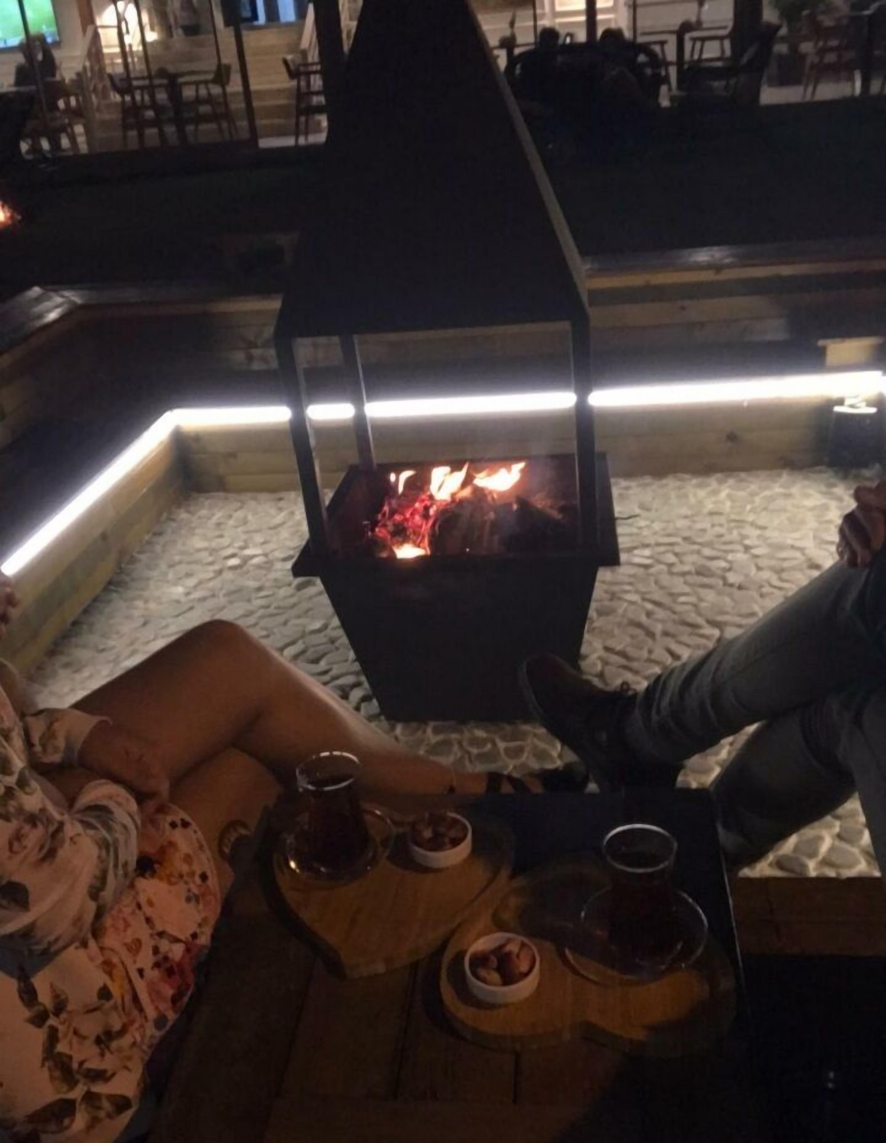 A cozy outdoor seating area with a built-in fire pit, surrounded by stone flooring and wooden furniture.
