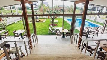 A spacious indoor area with a view of a swimming pool and a well-maintained garden.