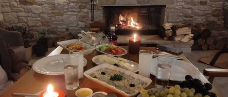 A cozy dining area with a stone fireplace, a table set with various dishes, glasses, and a candle.
