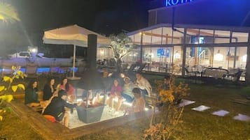 An outdoor seating area with a fire pit, surrounded by chairs and tables, in front of a building with a sign reading "ROYALOVA".