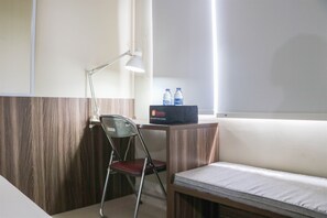 A hotel room with a wooden desk, a foldable chair, a bed, and a nightstand.
