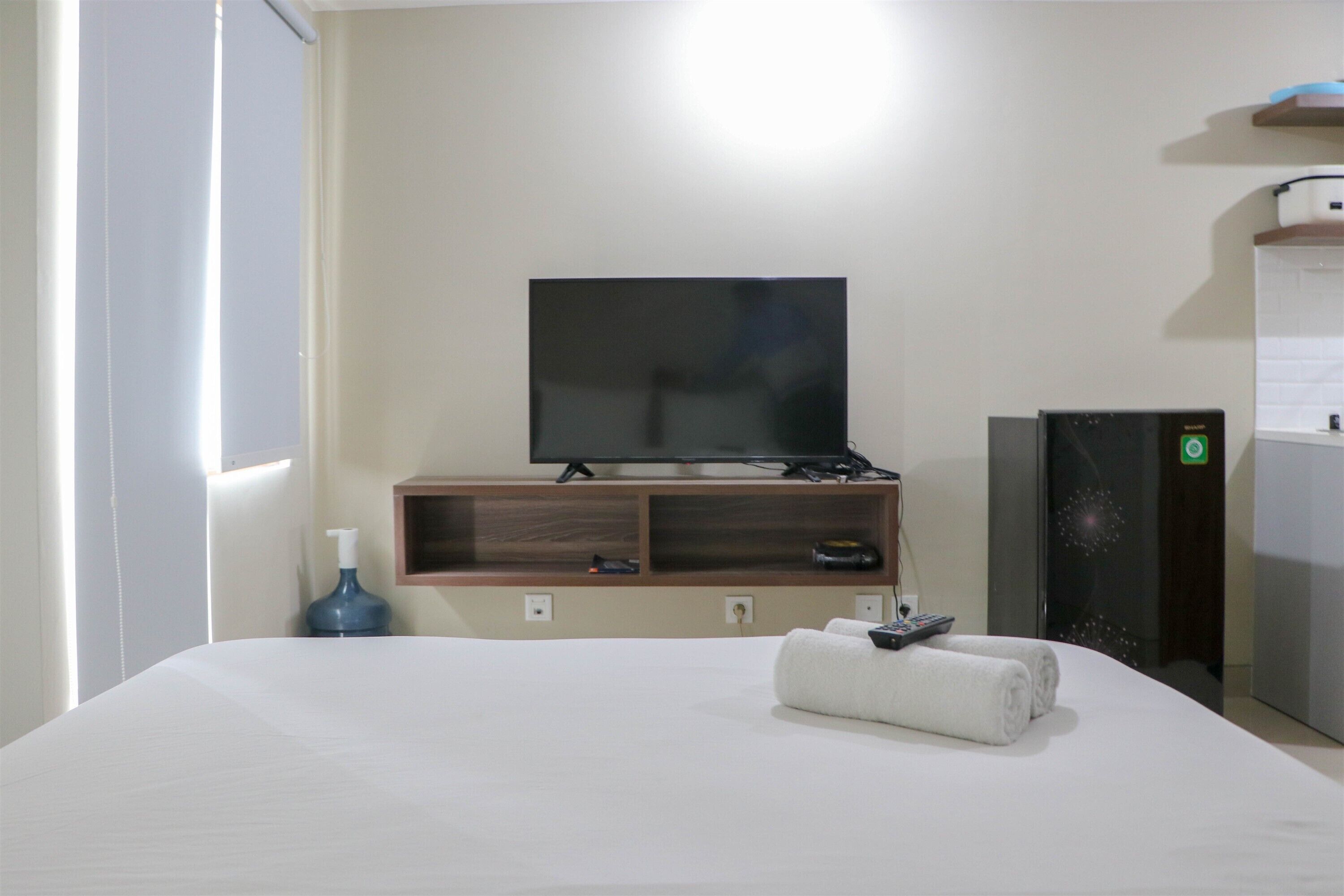 A hotel room with a bed, a flat-screen TV, a minibar, and a small desk with a remote control.