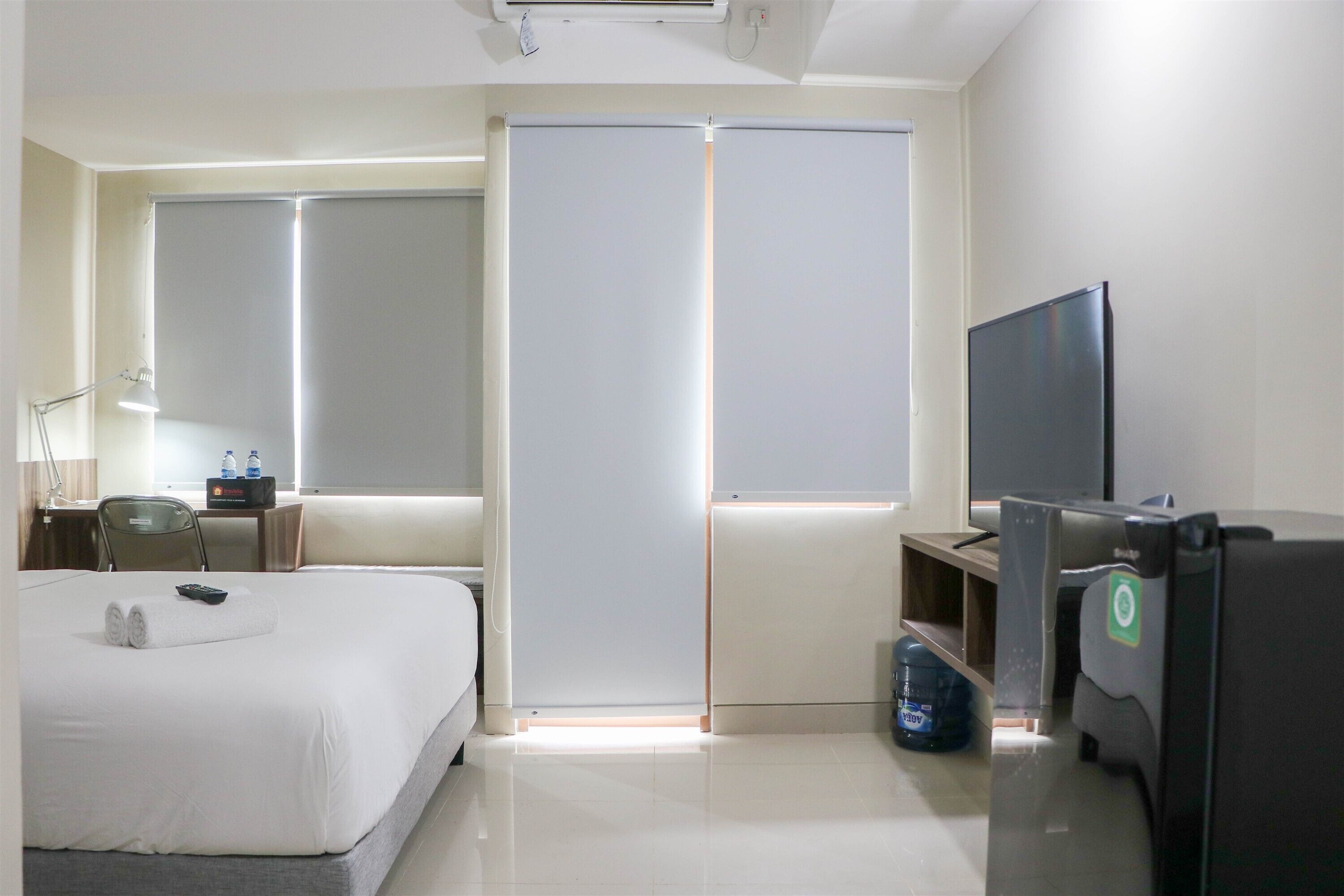 A hotel room with a bed, a desk with a computer, a TV, and a wardrobe.
