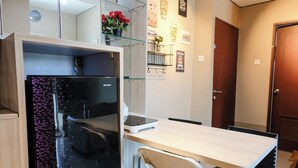 A compact room with a small desk, a chair, a refrigerator, and a glass shelf with flowers. - Best Choice 2Br Apartment At Taman Melati Jatinangor (Hegarmanah)