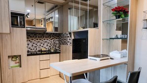 A modern kitchen with a microwave, stove, and black refrigerator. There is a wooden table with chairs and a small shelf with red flowers. - Best Choice 2Br Apartment At Taman Melati Jatinangor (Hegarmanah)