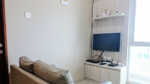 A modern living room with a sofa, a flat-screen TV mounted on a wooden cabinet, and a small shelf with decorative items. - Best Choice 2Br Apartment At Taman Melati Jatinangor (Hegarmanah)