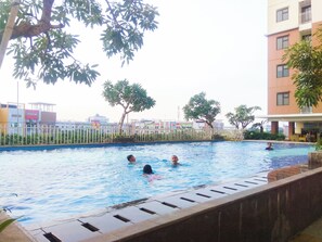 A swimming pool with people in the water, surrounded by buildings and trees. - Comfortable and Tidy 2BR Lagoon Bekasi Town Square Apartment (Bekasi)