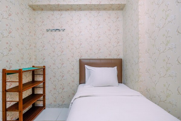 A small, neatly arranged bedroom with a single bed, a wooden shelf unit, and floral wallpaper. - Comfortable and Tidy 2BR Lagoon Bekasi Town Square Apartment (Bekasi)
