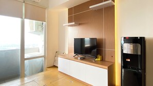 A modern kitchen with a flat-screen TV, a built-in refrigerator, and a sliding glass door leading to a balcony. - Nice And Cozy Studio Apartment At Vasanta Innopark (Cikarang)